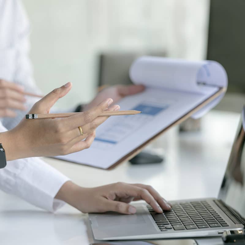 Cropped shot of business people hands holding pencil and using laptop computer while sitting at the table in office.